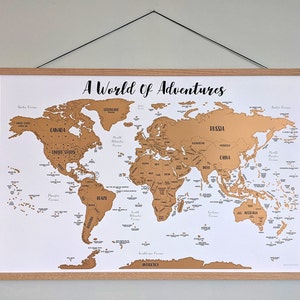 May include: A world map with a gold scratch-off surface, mounted on a white background. The map is labeled with country names and features the text "A World of Adventures" in a script font. The map is held by wooden bars.