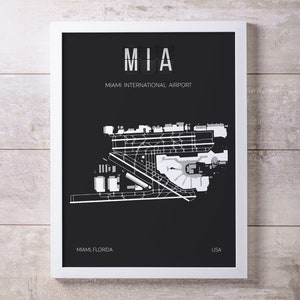 May include: Black and white airport map print with the text "MIA" and "Miami International Airport" in a white box. The map shows the layout of the airport with runways, taxiways, and terminals. The text "Miami, Florida" and "USA" are at the bottom of the print.