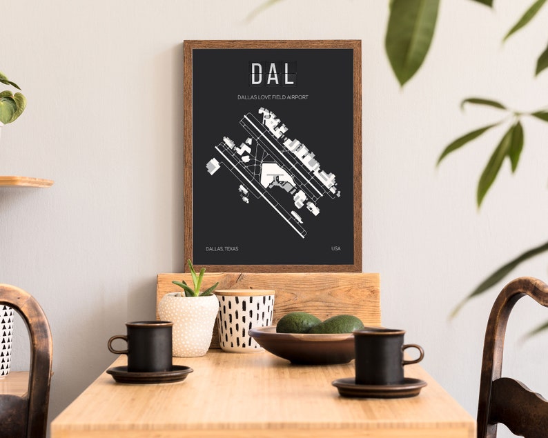 Puede incluir: Una impresi&oacute;n en blanco y negro del dise&ntilde;o del Aeropuerto Dallas Love Field con el c&oacute;digo del aeropuerto "DAL" y el nombre del aeropuerto "Dallas Love Field Airport" en texto blanco. La impresi&oacute;n est&aacute; enmarcada en un marco de madera marr&oacute;n y est&aacute; colgada en una pared blanca.