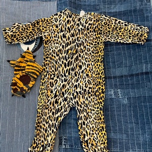 Puede incluir: Un mono de color amarillo y negro con estampado de leopardo, mangas largas y cierre de cremallera. El mono tiene un dobladillo y puños con volantes.