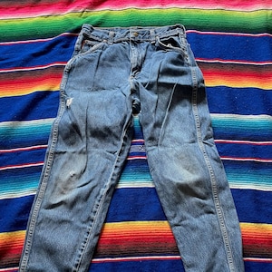 May include: A pair of blue denim jeans with a faded look and some wear and tear. The jeans have a straight leg and a classic five-pocket style.