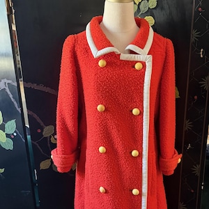 May include: A vintage red coat with a textured fabric, white trim, and yellow buttons. The double-breasted coat features a white collar and cuffs. The coat is displayed on a mannequin.