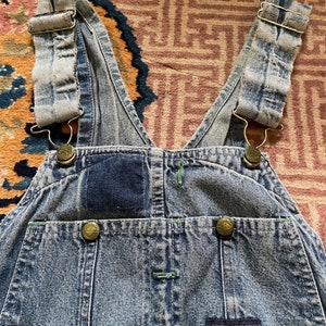 May include: Light blue denim dungarees with adjustable straps and a patch on the front that reads "OshKosh B'Gosh Union Made Sanforized".