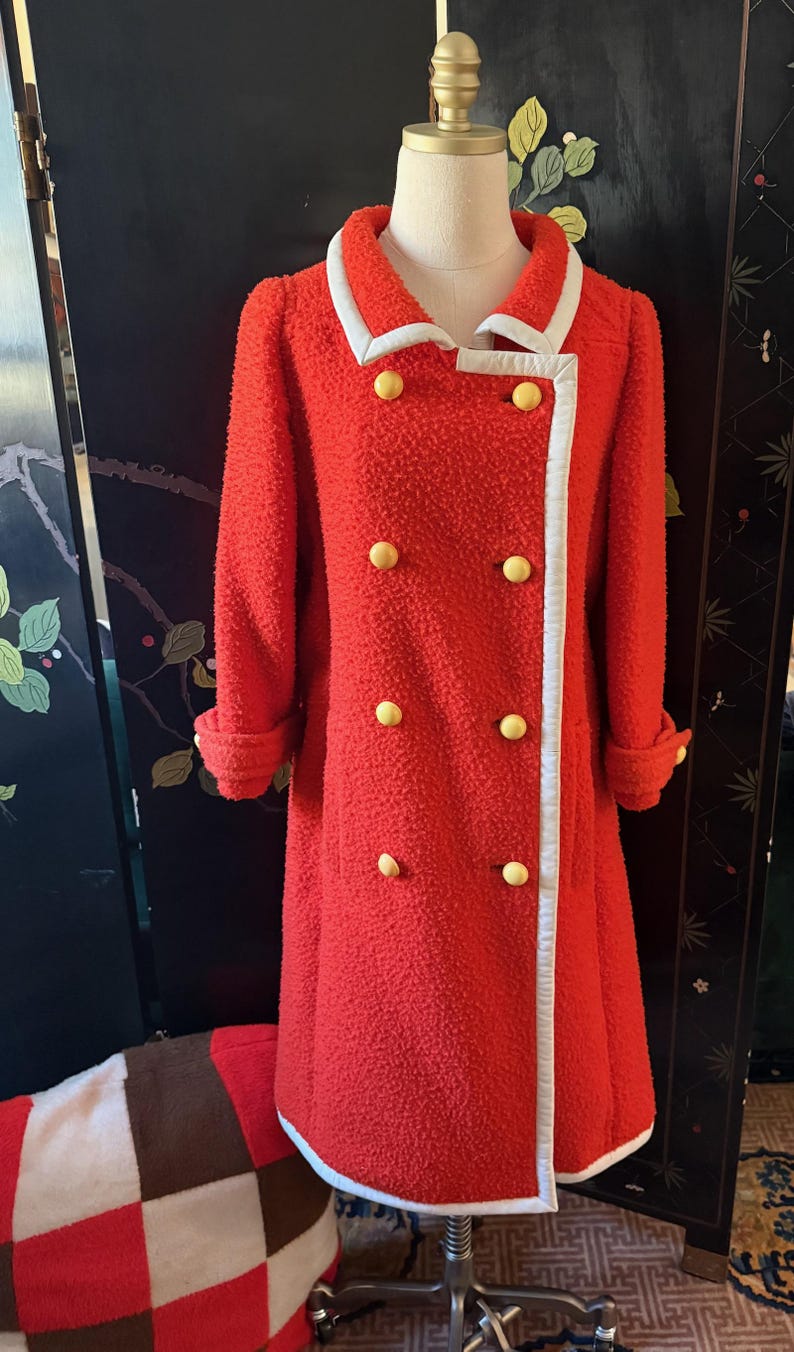 May include: A vintage red coat with a textured fabric, white trim, and yellow buttons. The double-breasted coat features a white collar and cuffs. The coat is displayed on a mannequin.