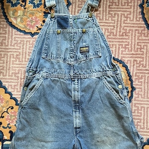 May include: Light blue denim dungarees with a distressed hem. The dungarees have a patch pocket on the chest and a brand label that reads "Dickies" on the right side of the waist.