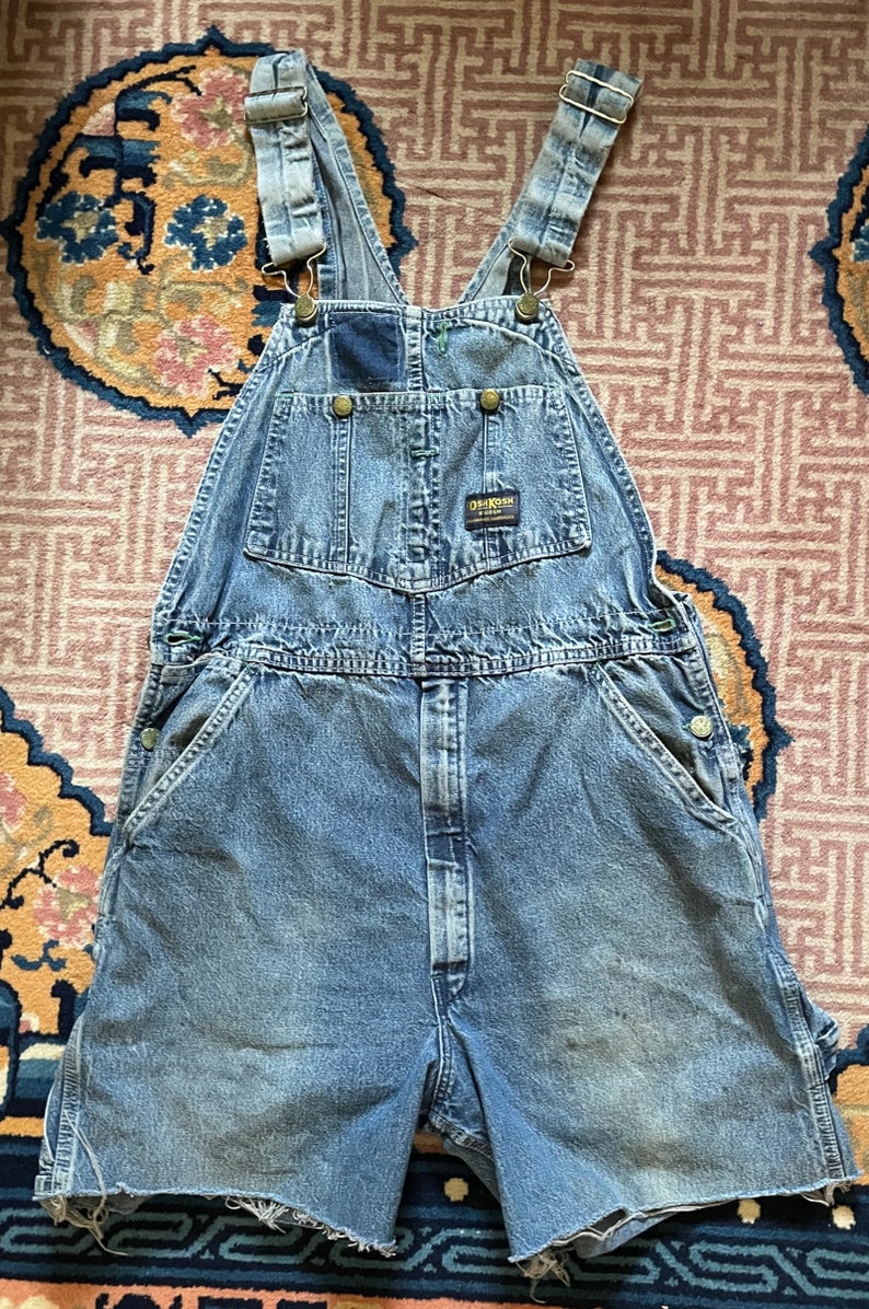 May include: Light blue denim dungarees with a distressed hem. The dungarees have a patch pocket on the chest and a brand label that reads "Dickies" on the right side of the waist.