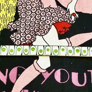 Könnte beinhalten: Ein Vintage-Armband mit weißer Basis, das grüne und weiße kreisförmige Designs aufweist. Das Armband hat einen goldfarbenen Verschluss und ist vor einem schwarzen Hintergrund mit rosa Text und Illustrationen platziert. Ein Retro-Accessoire.