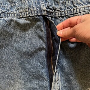 May include: Close-up of a blue denim zipper with a gold zipper pull. The zipper is partially open and the fabric is slightly creased.