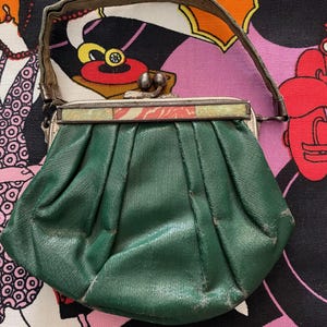 Könnte beinhalten: Eine kleine, grüne Ledertasche mit einem silbernen Verschluss und einem dekorativen, mehrfarbigen Blumendesign auf der Vorderseite.