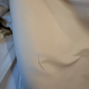 May include: Close-up of a light beige fabric with a subtle sheen. The fabric is slightly wrinkled, with a visible seam and the text "Samuel Robe" on a label.