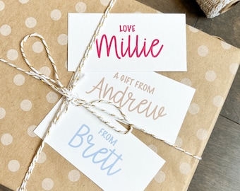May include: A brown gift box with white polka dots is wrapped with white twine and three gift tags. The top tag says "Love Millie" in pink script. The middle tag says "A gift from Andrew" in brown script. The bottom tag says "From Brett" in blue script.