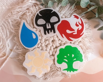May include: Five round stickers with different symbols representing the elements of earth, fire, water, air, and death. The stickers are white with black, red, blue, yellow, and green symbols.