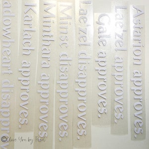 May include: A set of white vinyl stickers with the names of characters from the game Baldur's Gate 3. The stickers say "Astarion approves", "Lae'zel approves", "Gale approves", "Lae'zel disapproves", "Minse disapproves", "Minthara approves", "Karlach approves", and "Shadowheart disapproves".