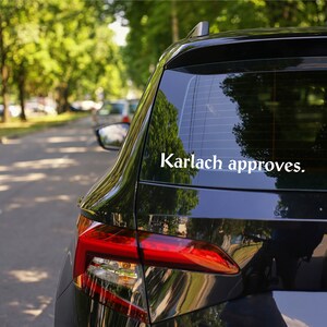 May include: A black car with a white sticker on the back window that says "Karlach approves."