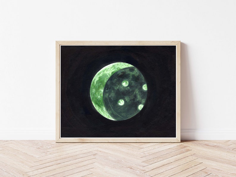 May include: A framed watercolor painting of a crescent moon with a green glow and dark craters. The moon is set against a black background.