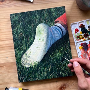 May include: A close-up of a white sock with a blue stripe, lying on a bed of green grass. The sock is painted with a realistic style, showing the texture of the fabric and the details of the stitching.