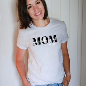 Pu&ograve; includere: Maglietta bianca con testo nero che dice "MOM caleb lilly david EST. 2011"