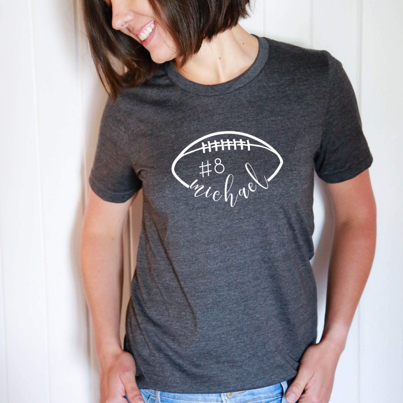 May include: A dark gray t-shirt with a white football graphic and the text "#8 michael" on the front.