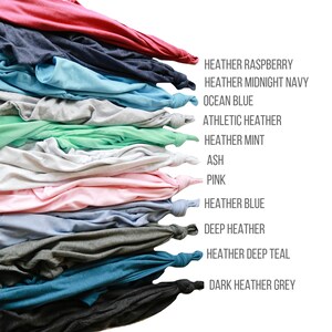 K&ouml;nnte beinhalten: Ein Stapel gefalteter T-Shirts in verschiedenen Farben, darunter Heidelbeer-Melange, Mitternachtsblau-Melange, Ozeanblau, Sport-Melange, Minze-Melange, Asche, Rosa, Blau-Melange, Dunkel-Melange, Teal-Melange und Dunkelgrau-Melange.
