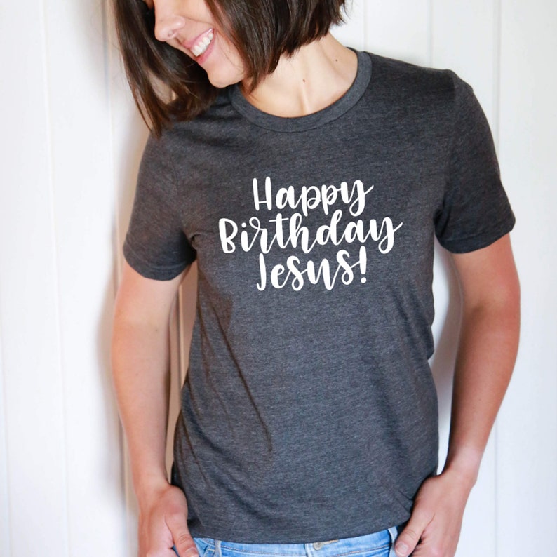 以下が含まれることがあります： 白い文字で「Happy Birthday Jesus!」と書かれた濃いグレーのTシャツです。