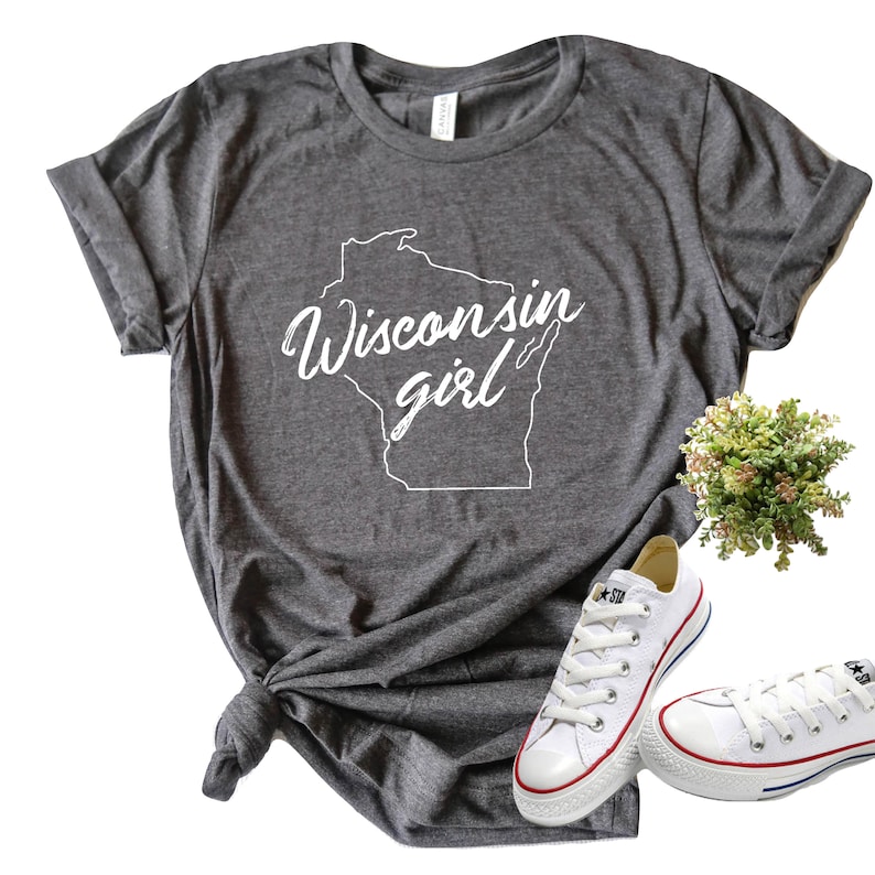 K&ouml;nnte beinhalten: Graues T-Shirt mit einem wei&szlig;en Umriss des Bundesstaates Wisconsin und dem Text "Wisconsin girl" in wei&szlig;er Kursivschrift.