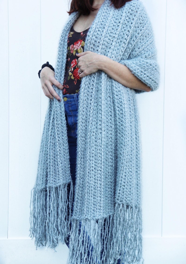 May include: A light blue crocheted scarf with fringe. The scarf is draped over a person's shoulders.