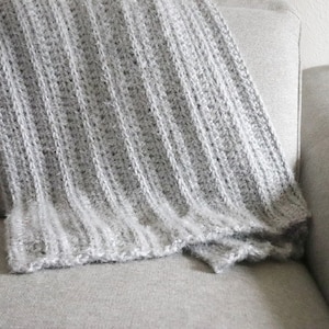 May include: A soft, gray knitted throw blanket draped over a couch.