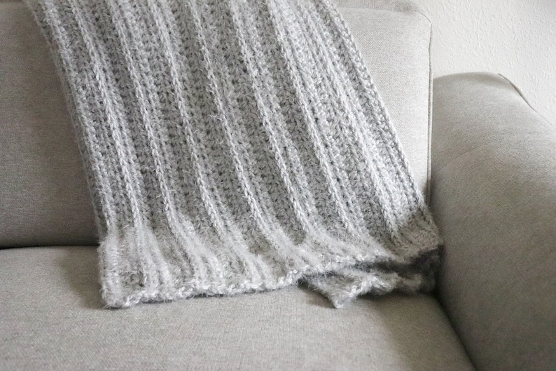 May include: A soft, gray knitted throw blanket draped over a couch.