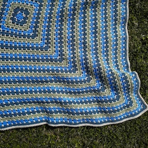 May include: A crocheted square blanket with a blue and green striped pattern. The blanket is made with a granny square stitch and has a white border.