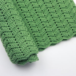 May include: A green crocheted blanket with a scalloped edge. The blanket is rolled up and the crocheted pattern is visible.