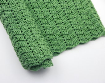 May include: A green crocheted blanket with a scalloped edge. The blanket is rolled up and the crocheted pattern is visible.