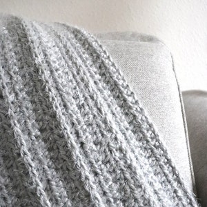 May include: A soft, gray crocheted throw blanket with a fuzzy texture. The blanket is draped over a light gray couch.