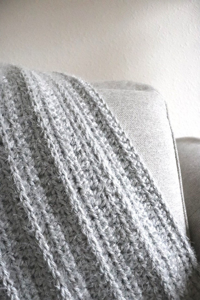 May include: A soft, gray crocheted throw blanket with a fuzzy texture. The blanket is draped over a light gray couch.