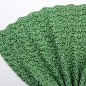 K&ouml;nnte beinhalten: Eine gr&uuml;ne H&auml;keldecke mit einem gewellten Rand. Die Decke ist mit einem einfachen Stichmuster gearbeitet und hat eine weiche, strukturierte Haptik.