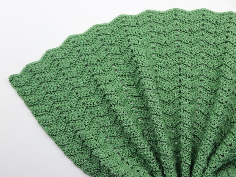 K&ouml;nnte beinhalten: Eine gr&uuml;ne H&auml;keldecke mit einem gewellten Rand. Die Decke ist mit einem einfachen Stichmuster gearbeitet und hat eine weiche, strukturierte Haptik.