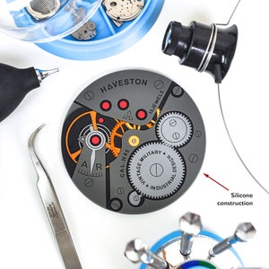 Puede incluir: Primer plano de un movimiento de reloj con el texto "HAVESTON 15 JEWELS CAL.H.45 VINTAGE MILITARY DESIGN * INDUSTRIAL" impreso en la esfera. El movimiento est&aacute; hecho de metal y tiene una combinaci&oacute;n de colores gris, naranja y rojo.
