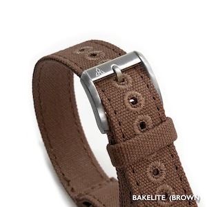 May include: A brown canvas watch strap with a silver buckle. The buckle has a triangle logo with the letters "A.S." inside. The strap is stitched with a decorative pattern.  BAKELITE (BROWN)