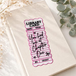 Op de afbeelding: Een rechthoekige boekenlegger in de vorm van een vintage bibliotheekkaart met geschulpte randen en een roze omlijning. De tekst bevat LIBRARY CARD, DATE, TITLE, NO. 061507 en de zin You had me at Chapter One, vergezeld van kleine hart- en strikiconen.