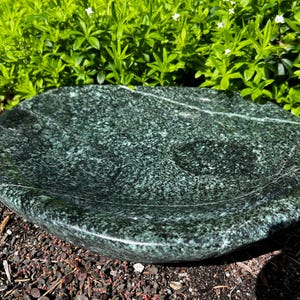 May include: A round, shallow bowl carved from dark green stone with a polished, speckled surface featuring natural white veining patterns throughout the material. The bowl has a smooth, curved rim and a wide, concave interior basin.