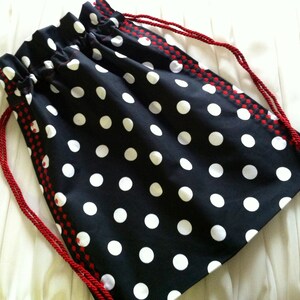 May include: A black and white polka dot drawstring bag with red trim. The bag has a white cord drawstring.