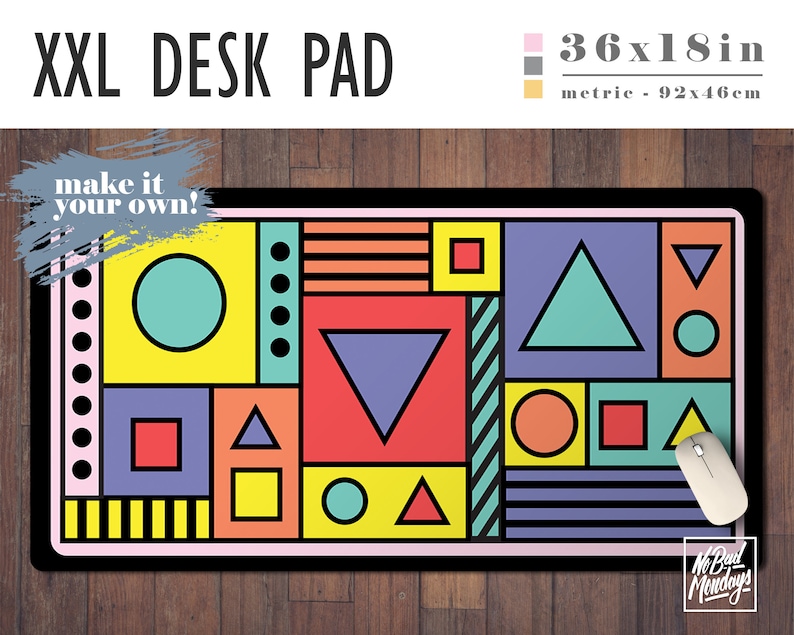 May include: A large geometric desk pad with a colorful design featuring circles, squares, triangles, and stripes. The pad is 36 inches by 18 inches and is made of a durable material. The text "make it your own!" is written in a white box on the top left corner of the pad. The text "No Bad Mondays" is written in a white box on the bottom right corner of the pad.