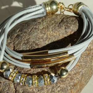 May include: A gray multi-strand bracelet with gold accents and crystal beads. The bracelet has a magnetic clasp.