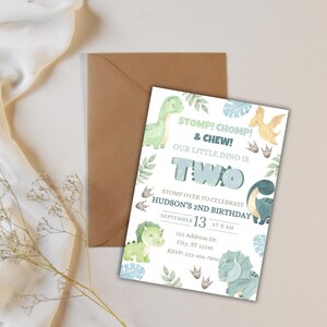 May include: A dinosaur-themed birthday invitation with the text "STOMP! CHOMP! & CHEW! OUR LITTLE DINO IS TWO." The invitation includes illustrations of dinosaurs and foliage, with the date and time of the party. A brown envelope is behind the invitation.