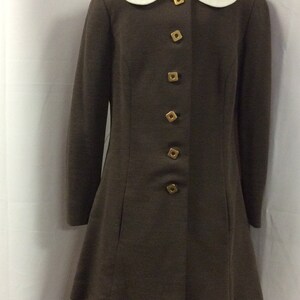 May include: A brown long-sleeved jacket with a white Peter Pan collar and gold buttons. The jacket has a slightly flared hem and is paired with matching brown pants.