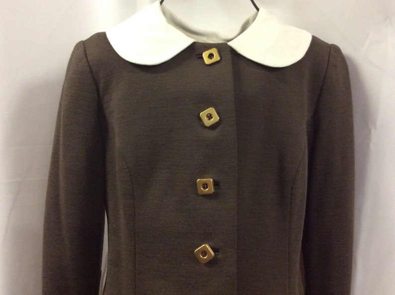 May include: A brown blazer with a white Peter Pan collar and gold square buttons.