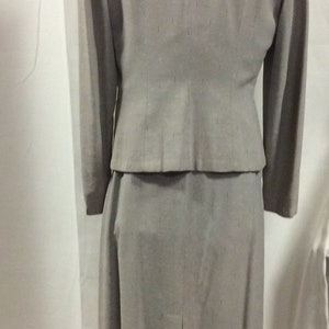 May include: A grey skirt suit with a fitted jacket and a straight skirt. The fabric has a subtle textured pattern.