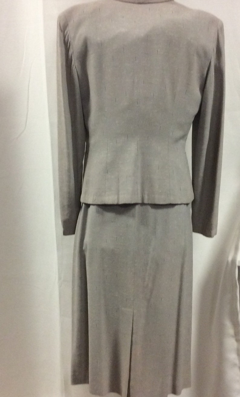 May include: A grey skirt suit with a fitted jacket and a straight skirt. The fabric has a subtle textured pattern.