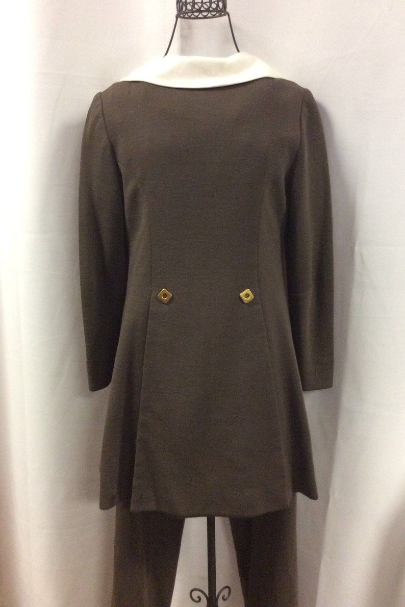 May include: A brown long-sleeved jacket with a white collar and two gold buttons on the back. The jacket is paired with matching brown pants.