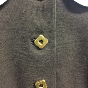 May include: A black collared shirt with three gold square buttons.