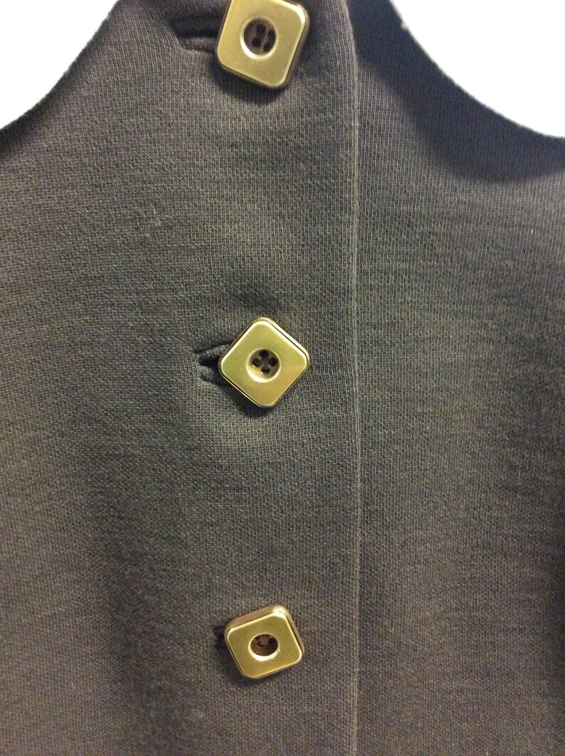 May include: A black collared shirt with three gold square buttons.